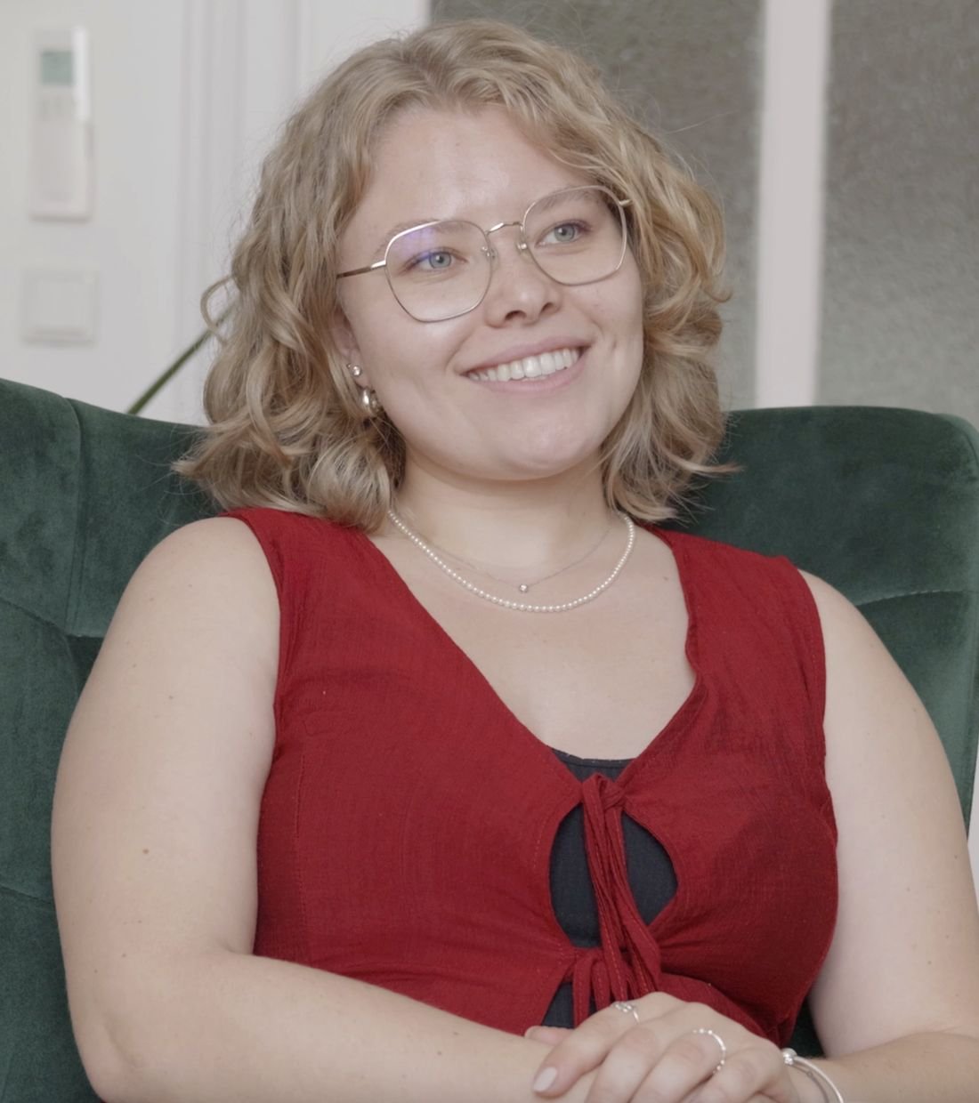 Nicole lächelnd in ihrem grünen Samtsessel in der Beratungspraxis